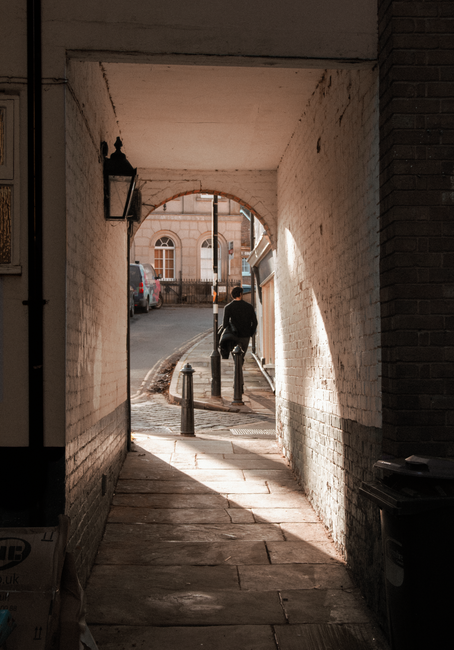 A narrow street in Erith's town centre with a clear blue sky overhead, featuring a variety of small shops and businesses housed in terraced buildings with different exterior finishes such as brick and